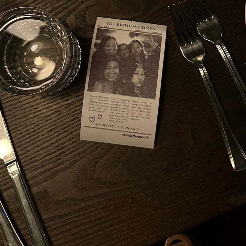 A newspaper-style printed photo on a dinner table beside cutlery and glasses