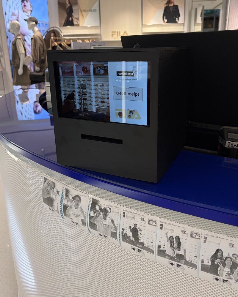 Black Receipt Booth on a Fila store counter, with printed photos along the front of the counter