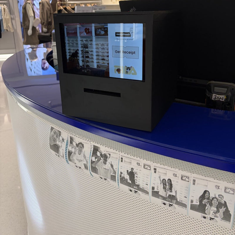 Black Receipt Booth on a Fila store counter, with printed photos below it