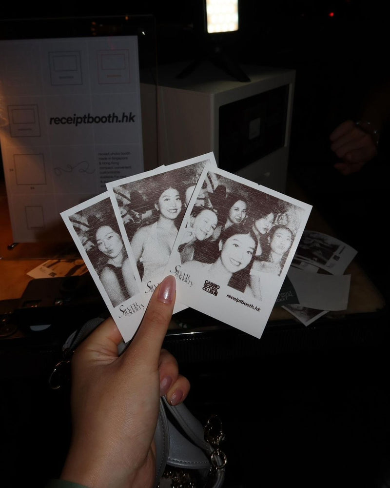 A hand holding three black and white printed photos at a night event