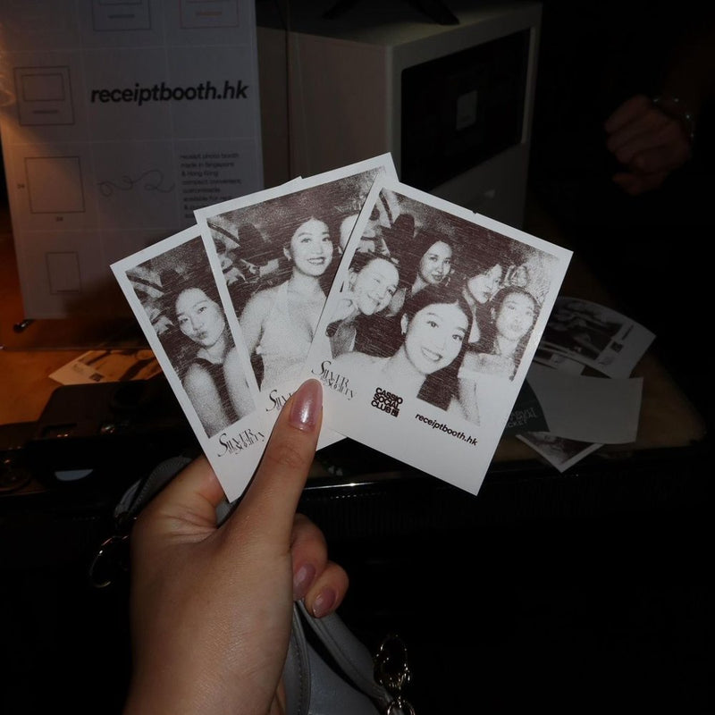 A hand holding three black and white printed photos at a night event
