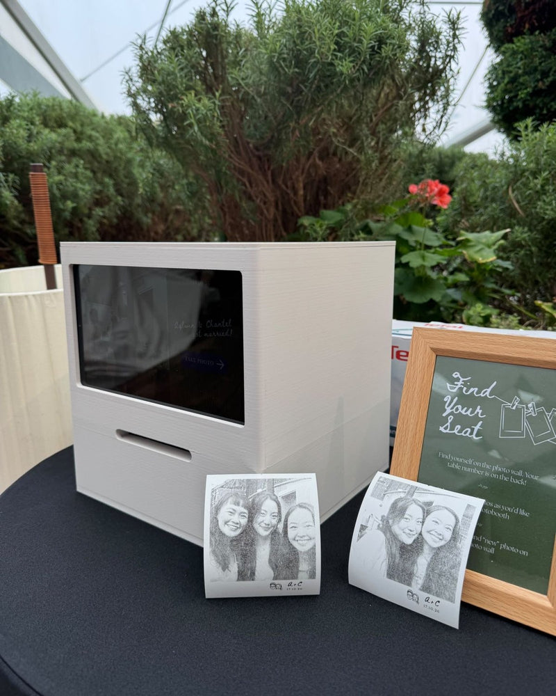 Cream Receipt Booth on a table in a glasshouse, with two printed photos in front and a framed seating sign beside it